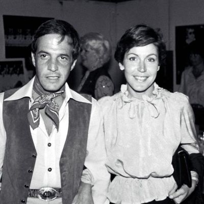 Jeff Wald is dressed as a cowboy as he and Helen Reddy are walking together in this monochrome image.